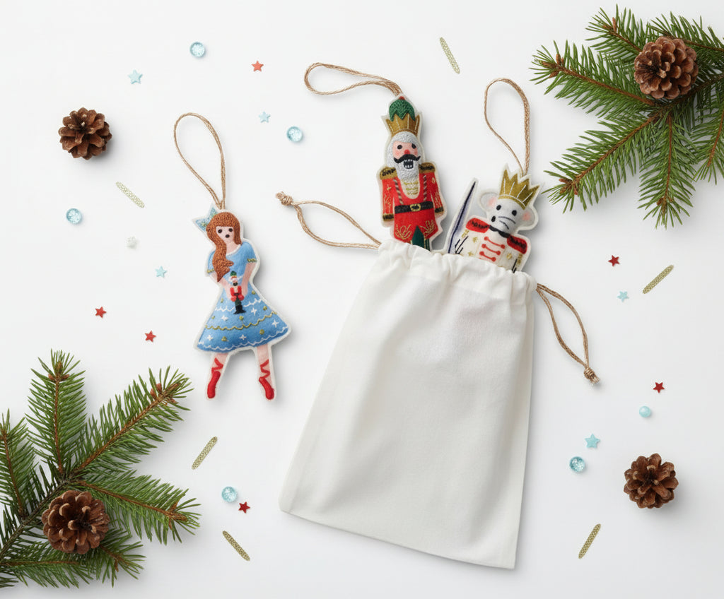 Decorative Christmas ornaments including a Nutcracker and a fairy, with a white drawstring bag on a white background.